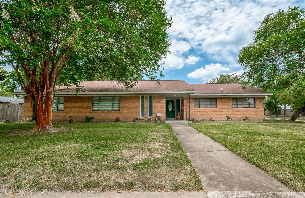 This is a single-story brick home featuring a large tree in the front yard, a well-kept lawn, and a pathway leading to the covered entrance.