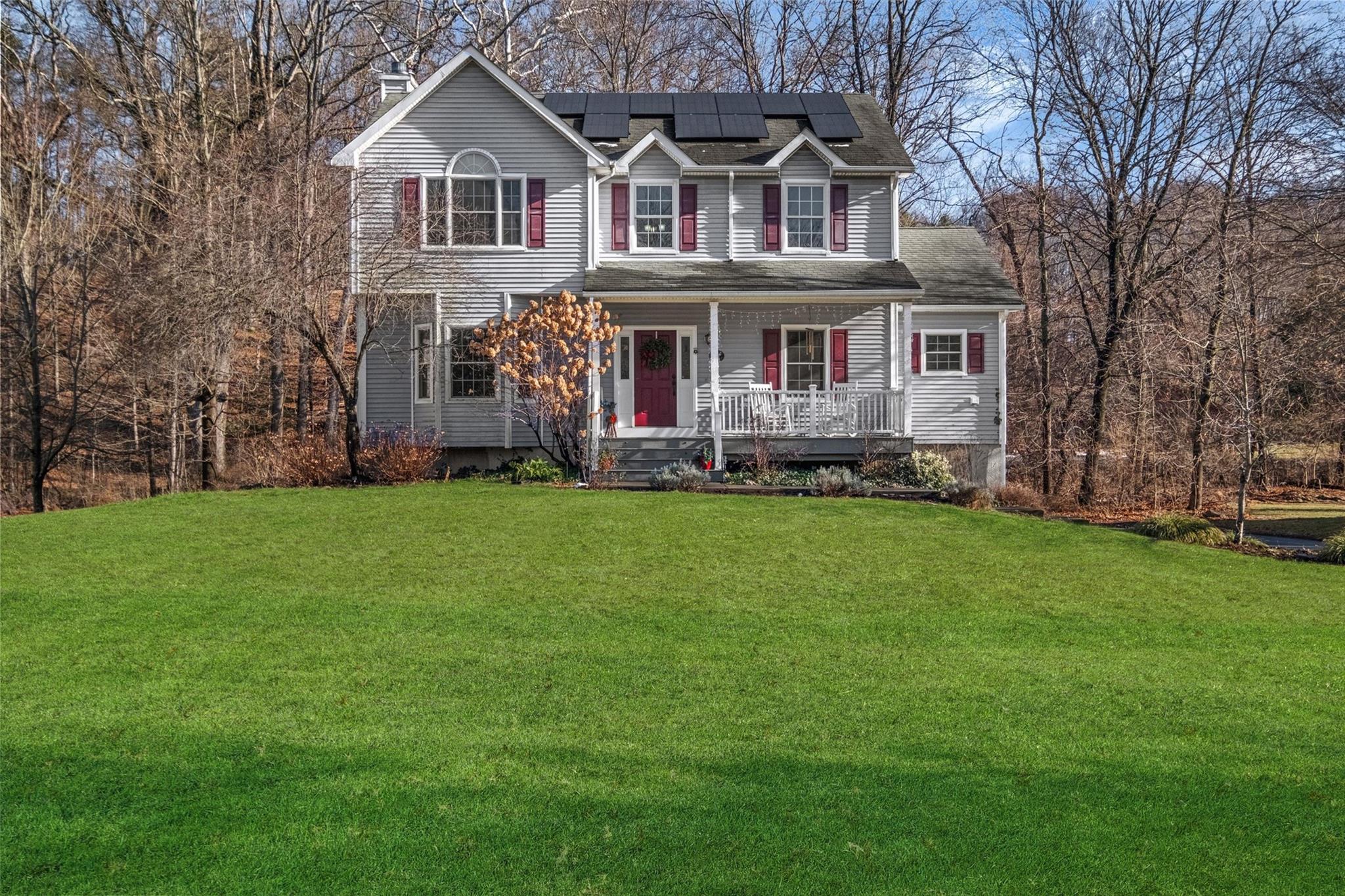 View of front of property with a front lawn, covered porch, and solar panels.