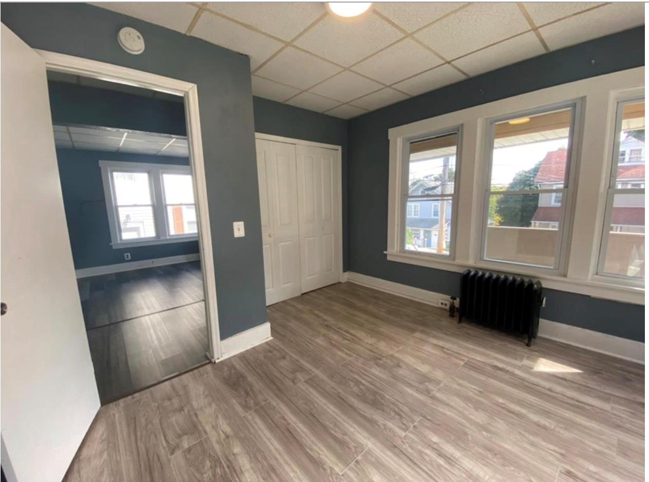 Unfurnished bedroom with multiple windows, radiator heating unit, wood-type flooring, and a drop ceiling