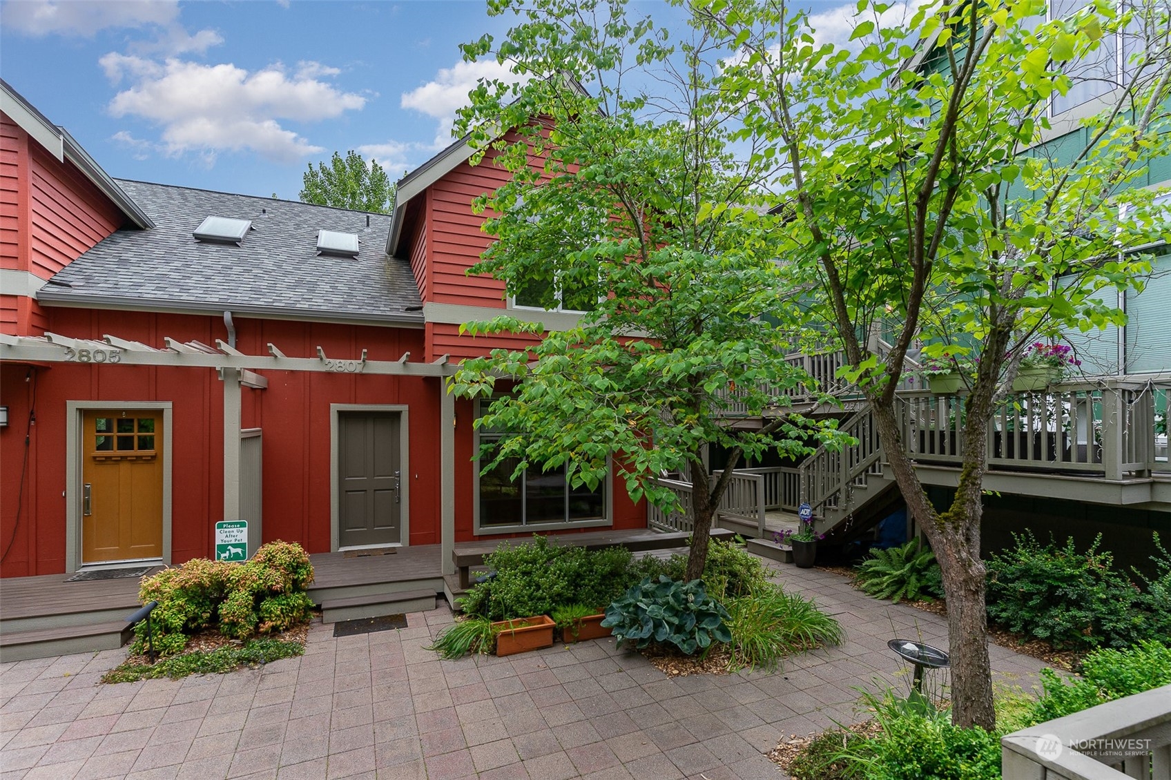 a view of a house with brick walls plants and large tree