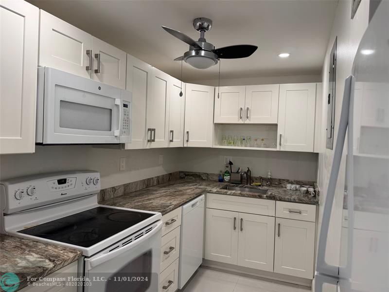 a kitchen with granite countertop white cabinets white stainless steel appliances and a sink