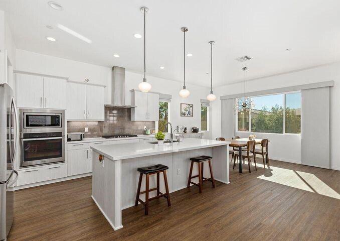 a open kitchen with stainless steel appliances granite countertop a stove a refrigerator a kitchen island a dining table and chairs with wooden floor