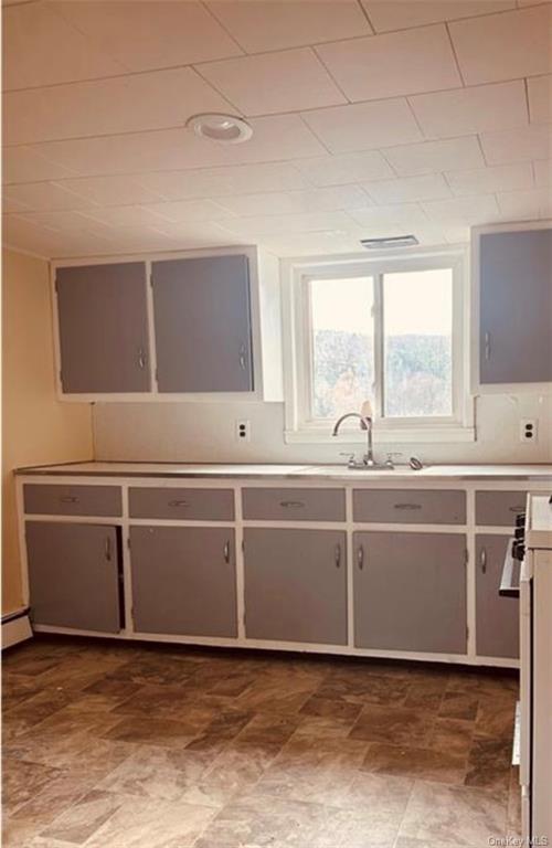 Kitchen with gray cabinets, a baseboard radiator, sink, and stainless steel range oven