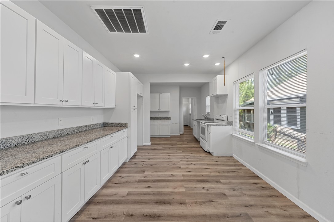 a large white kitchen with granite countertop a large counter top and stainless steel appliances