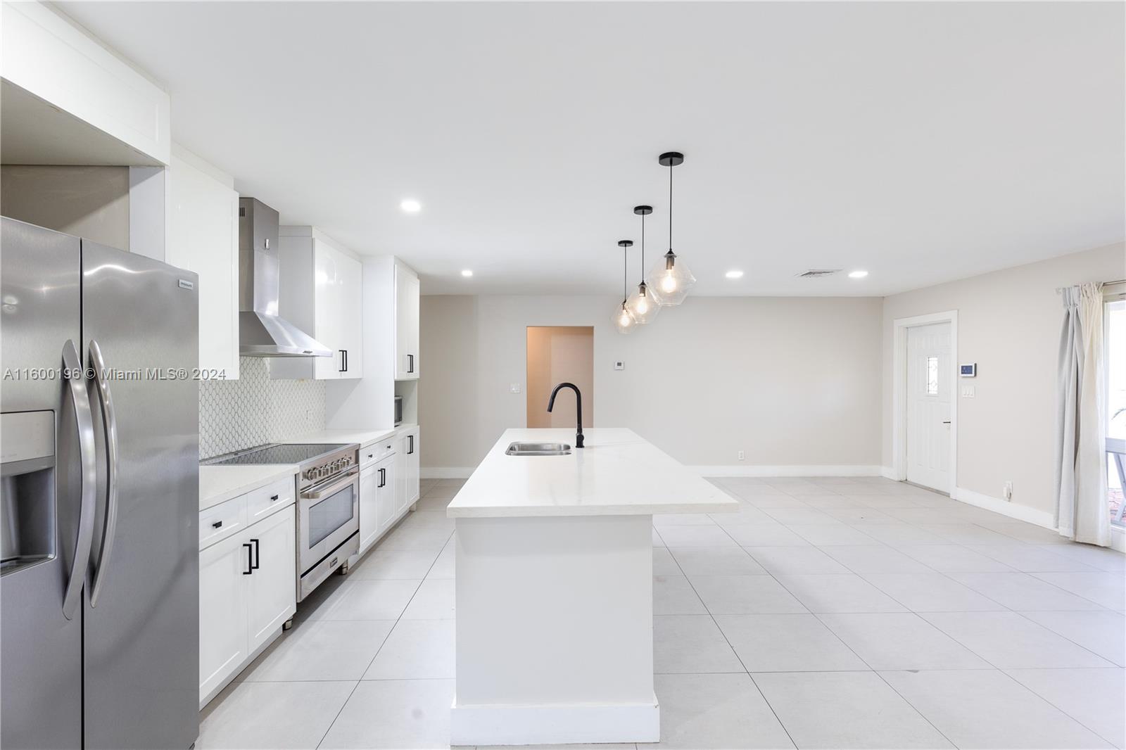 a large white kitchen with a large counter top a sink stainless steel appliances and cabinets