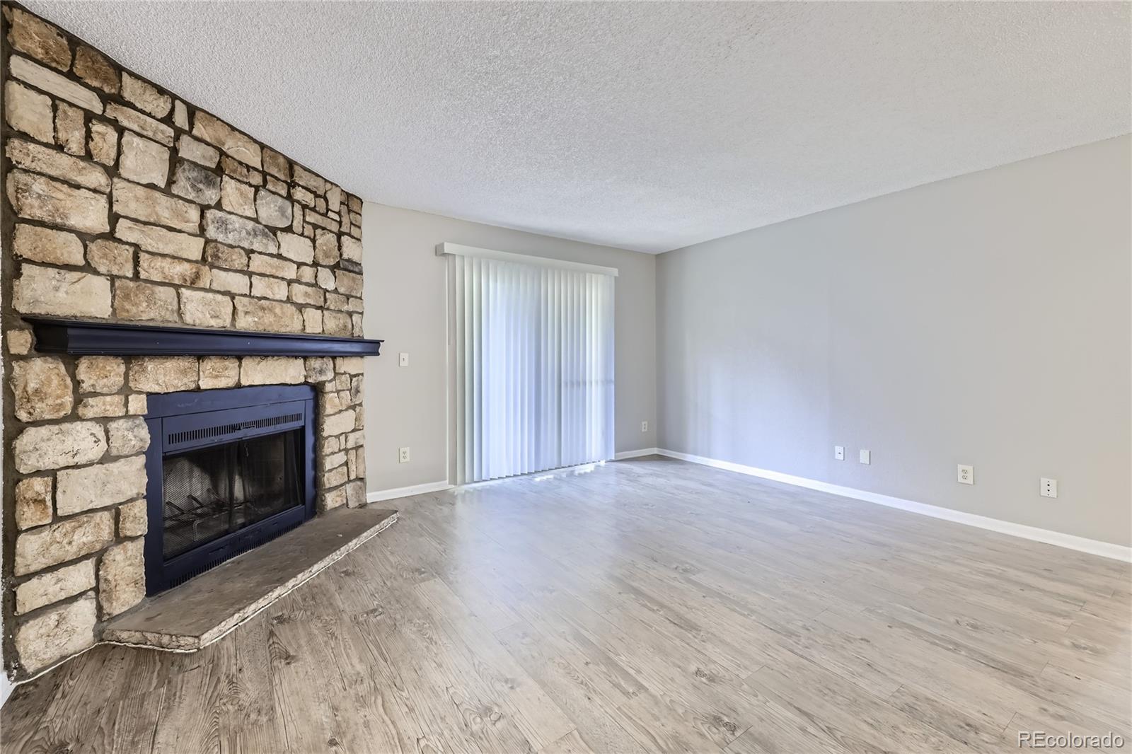 a view of an empty room with wooden floor fireplace and a window