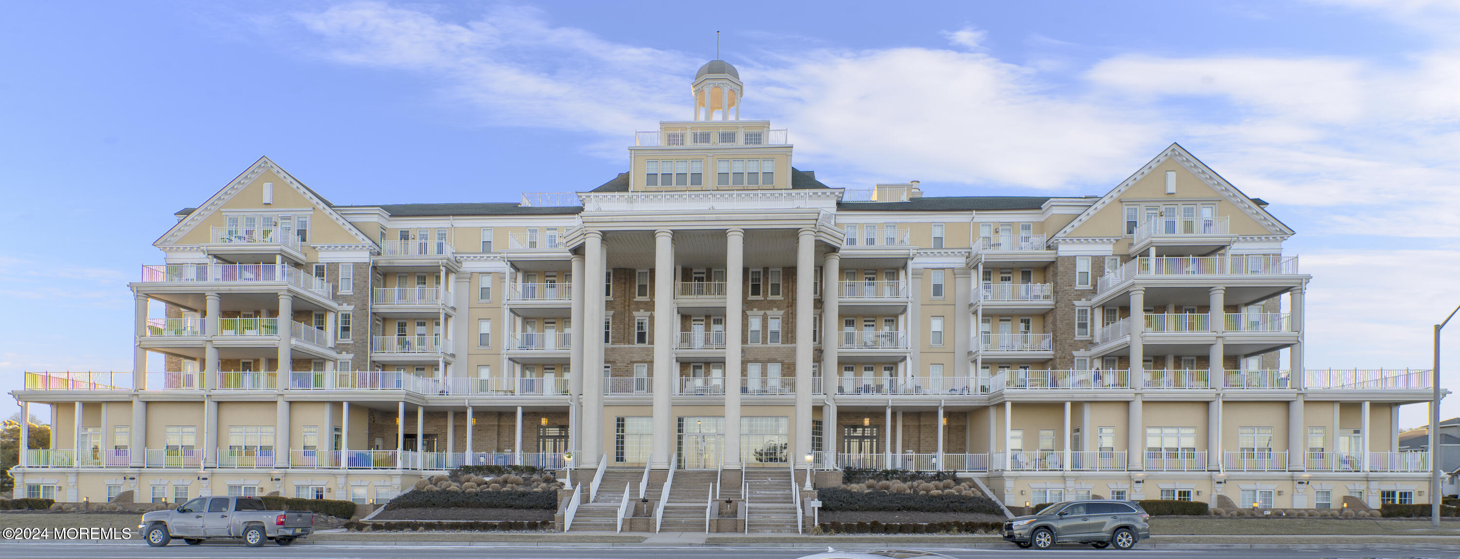 a front view of a building with lot of cars and trees