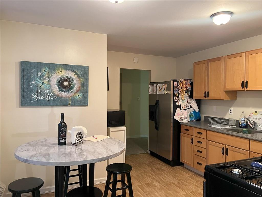 Kitchen with sink, stainless steel fridge with ice dispenser, black range, light brown cabinetry, and light hardwood / wood-style floors