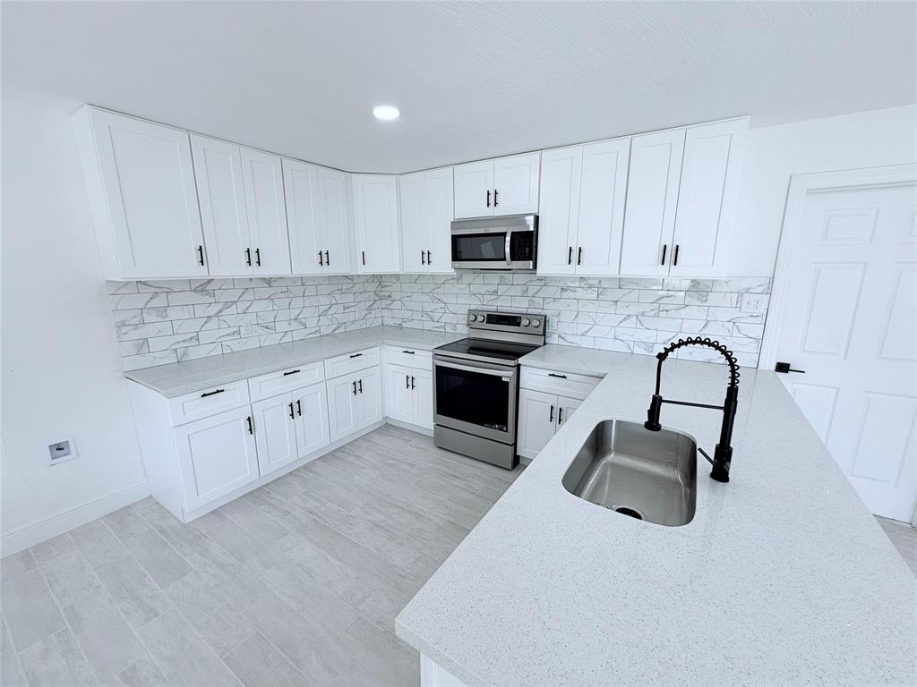 a kitchen with stainless steel appliances granite countertop a stove top oven a sink and white cabinets