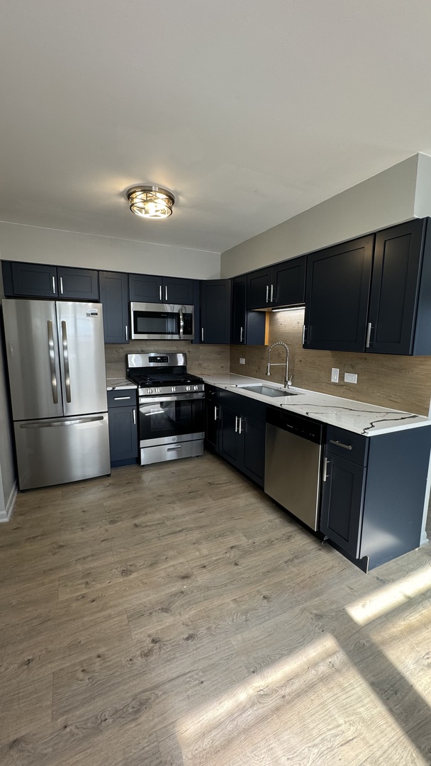 a kitchen with kitchen island stainless steel appliances a sink cabinets and wooden floor