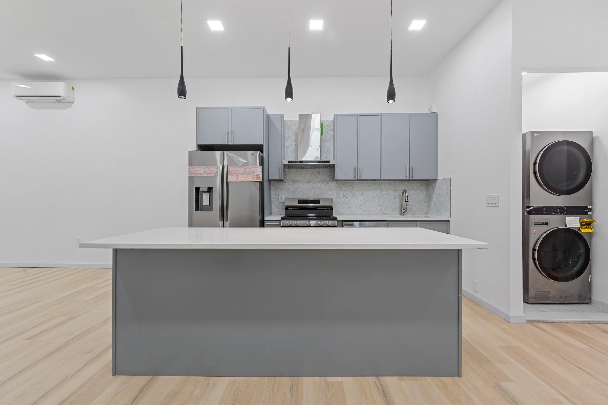 Kitchen featuring appliances with stainless steel finishes, wall chimney range hood, decorative light fixtures, an AC wall unit, and stacked washer / dryer