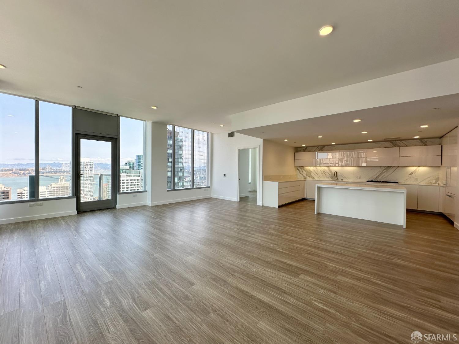 a view of an empty room with wooden floor and a kitchen