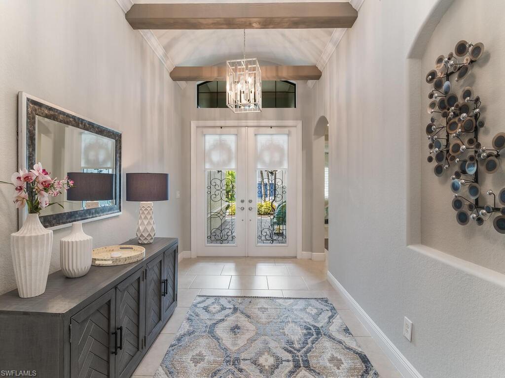 Foyer with french doors, a notable chandelier, light tile patterned flooring, and beam ceiling