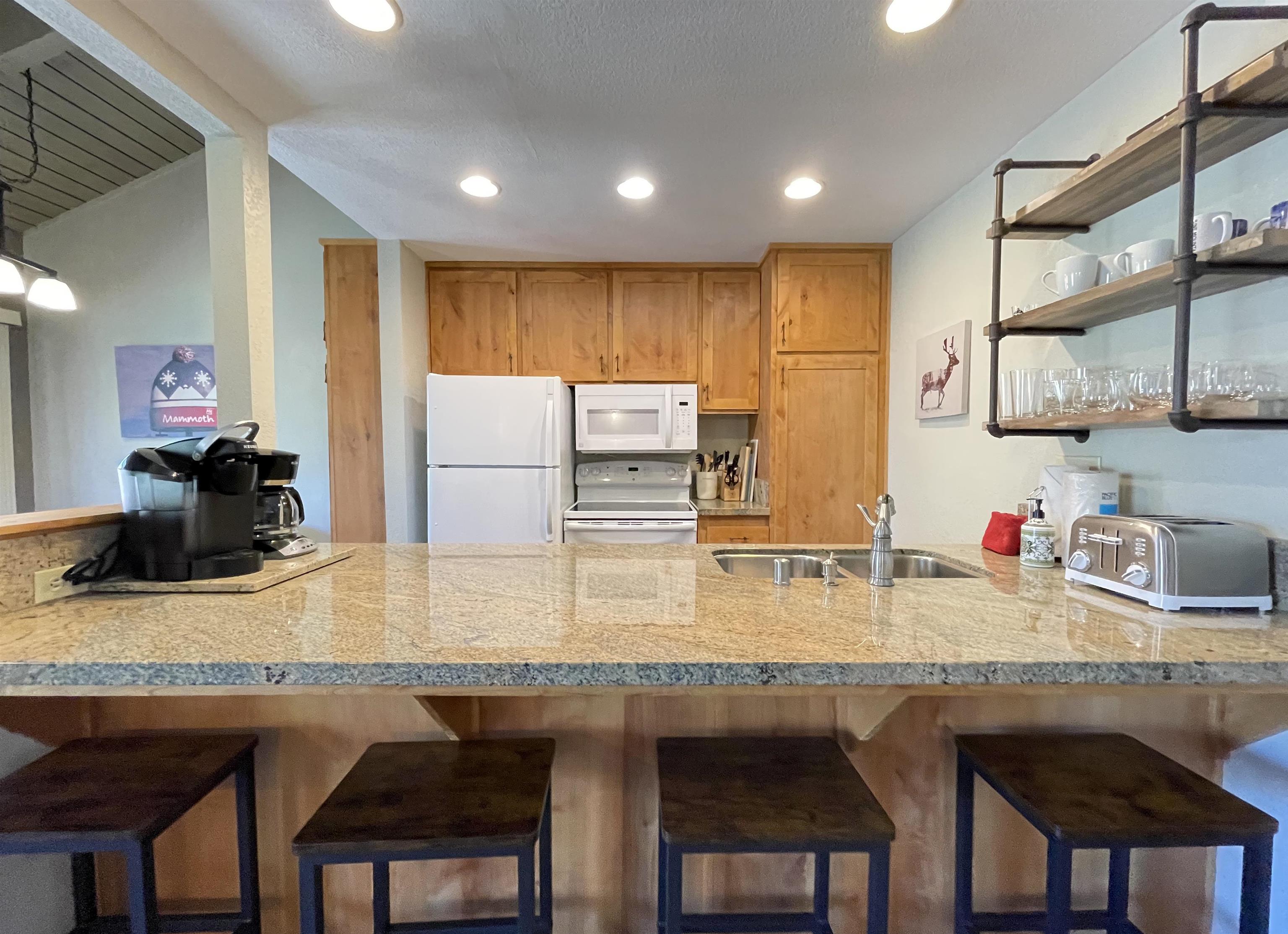 a kitchen with kitchen island granite countertop a table chairs sink refrigerator and microwave