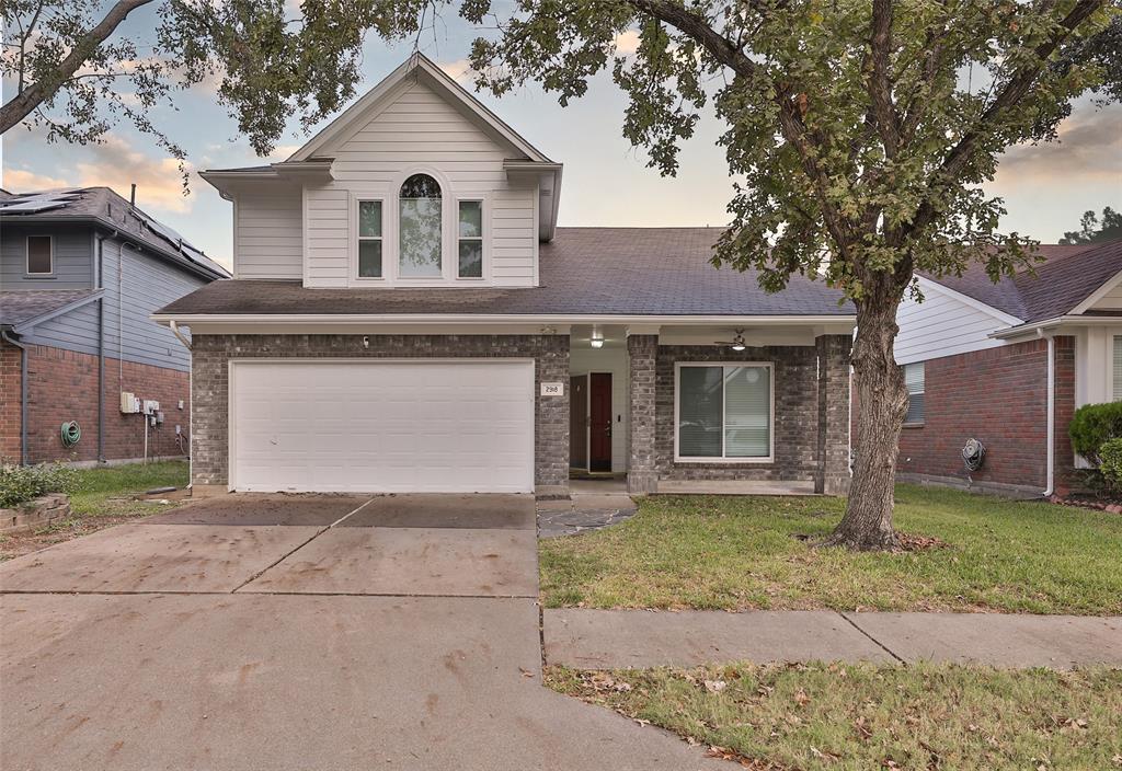 This is a two-story single-family home with a brick and siding exterior, featuring a two-car attached garage, a gabled roof, and a mature tree in the front yard.