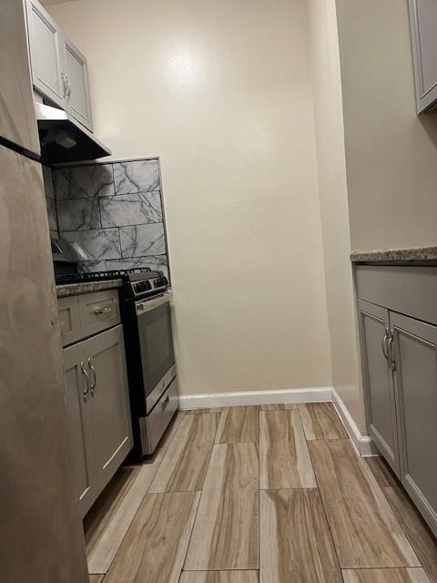 Kitchen with range, ceramic wood-style flooring, gray cabinetry, decorative backsplash, and exhaust hood