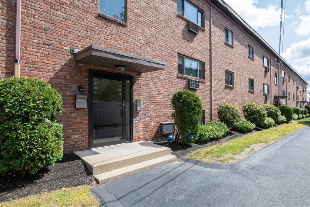 a view of a house with brick walls plants and large tree