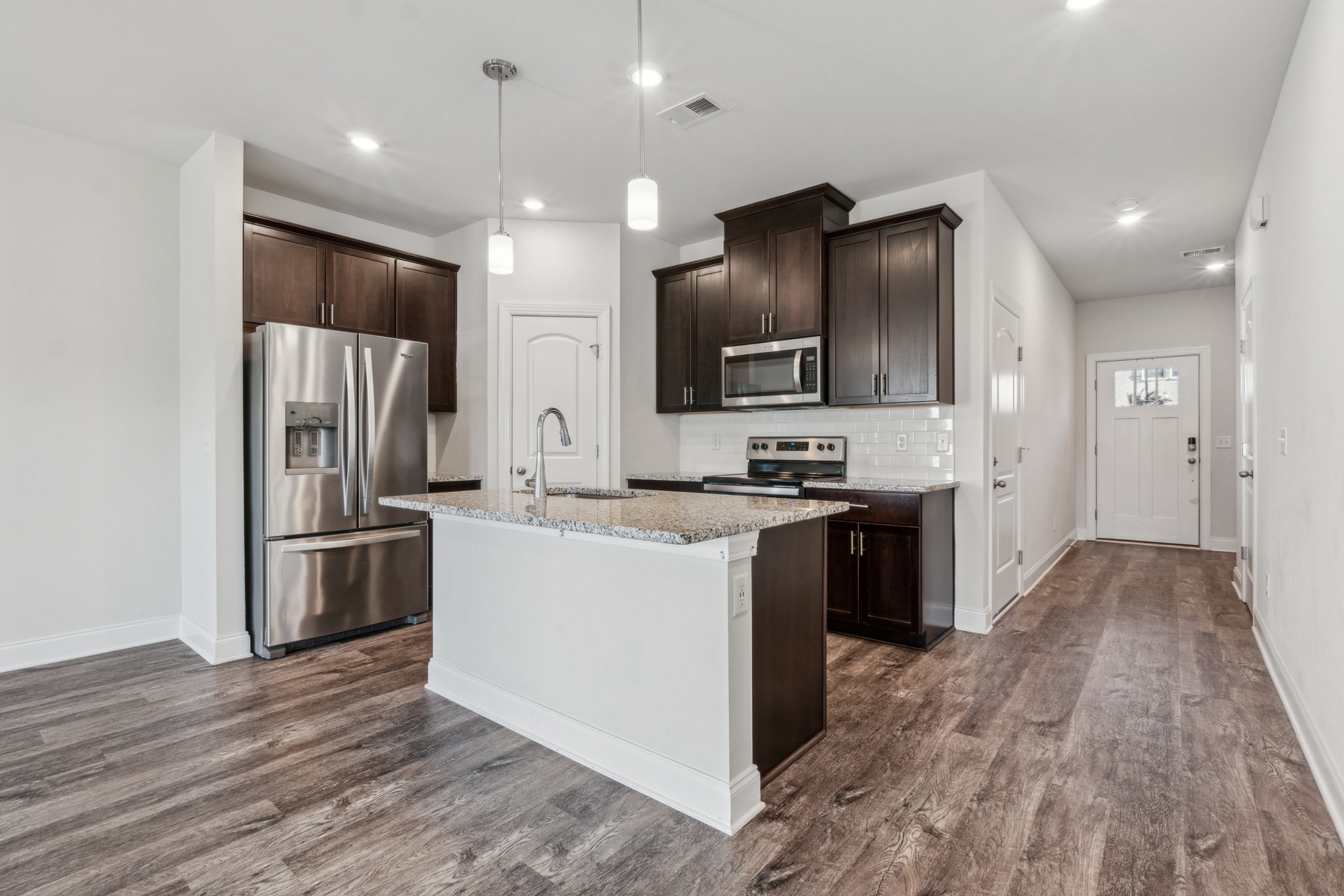 a kitchen with stainless steel appliances kitchen island granite countertop a refrigerator a stove top oven a sink and dishwasher with wooden floor