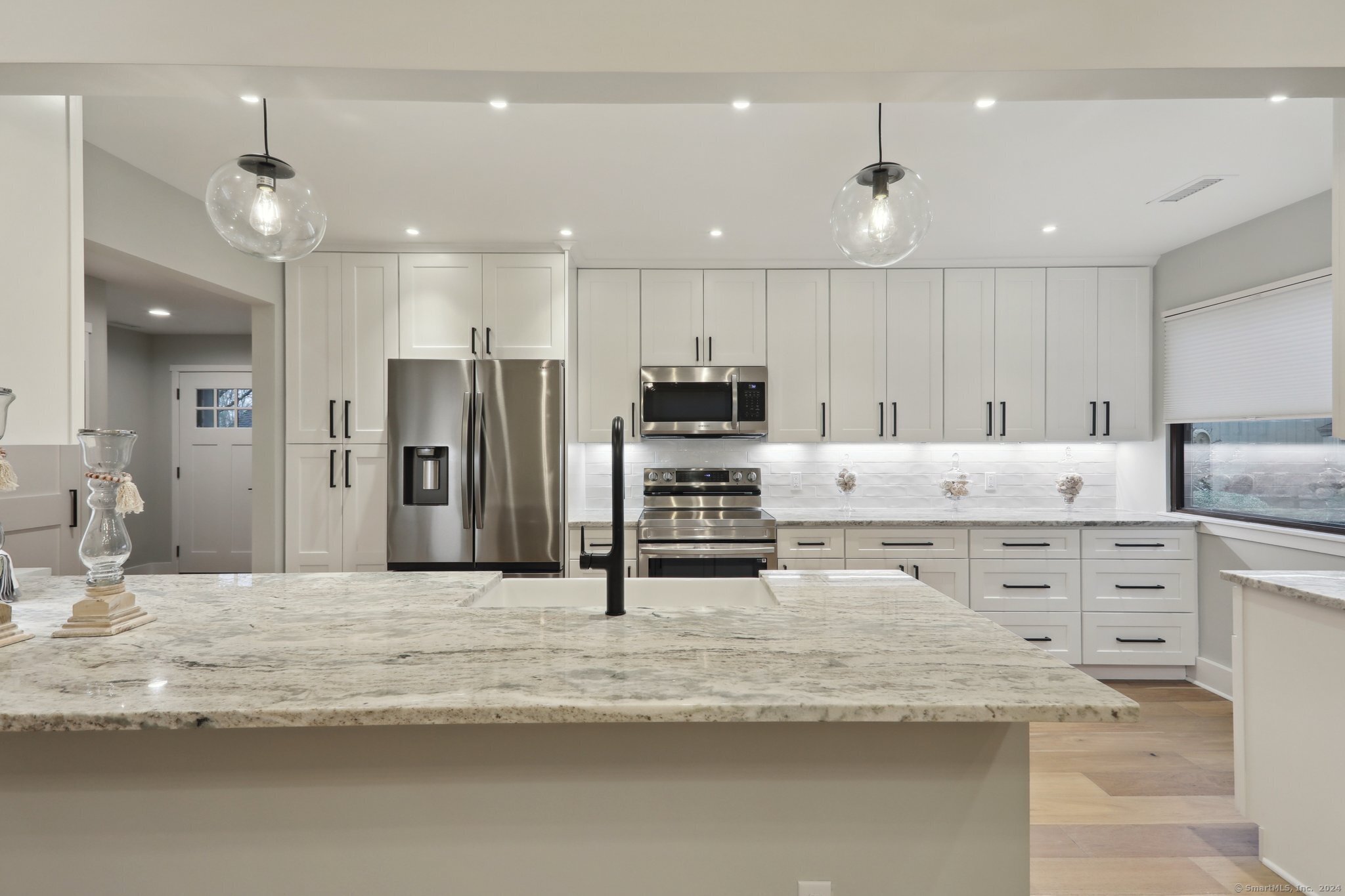 a large white kitchen with kitchen island a sink stainless steel appliances and cabinets