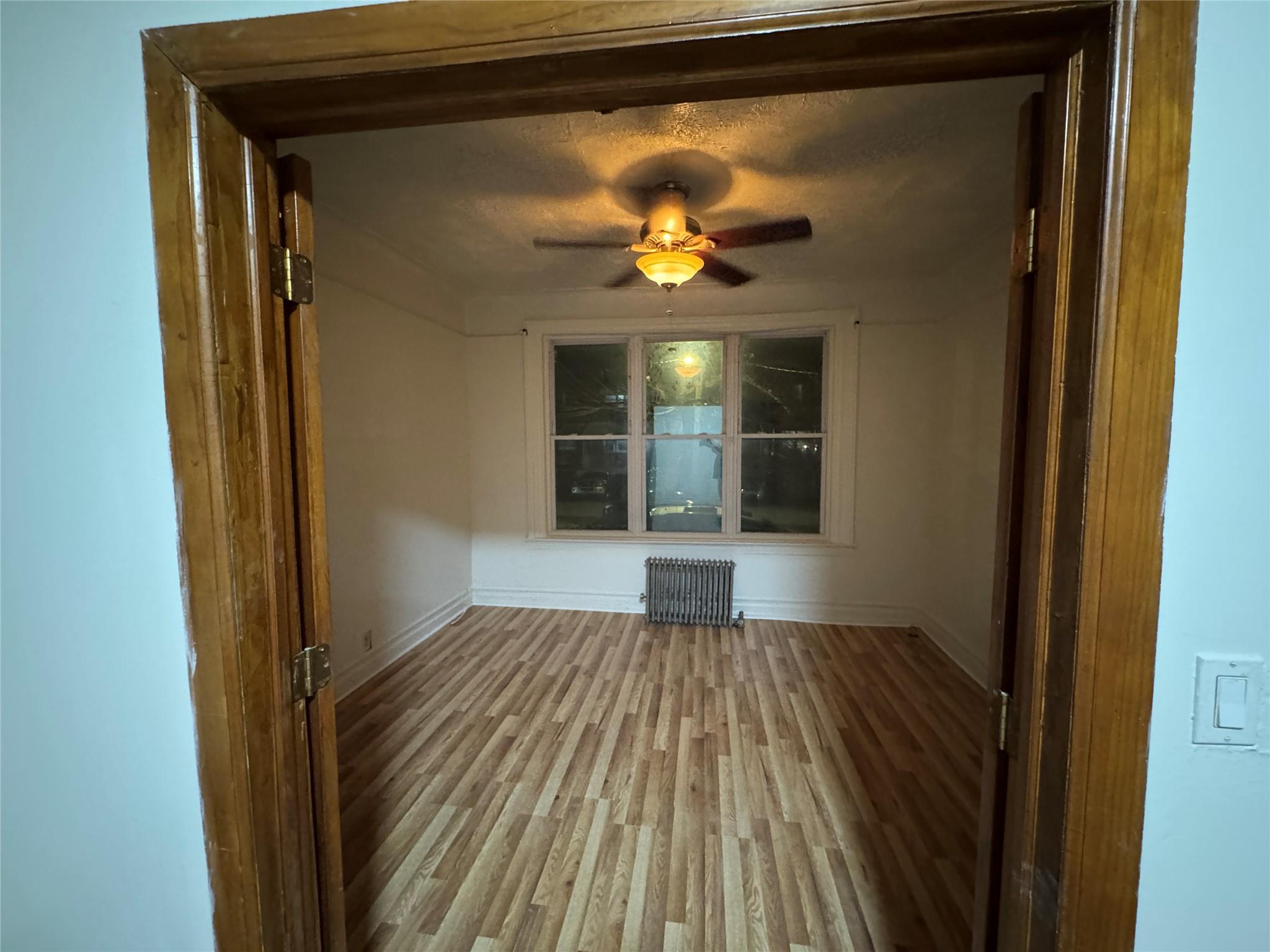 Unfurnished room with radiator, ceiling fan, wood-type flooring, and a textured ceiling