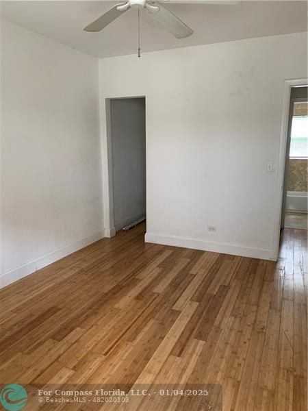 an empty room with wooden floor and fan