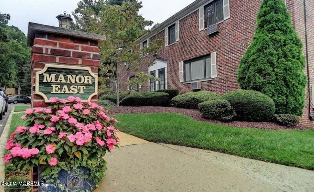 a sign that is sitting in front of a brick house with a big yard and potted plants