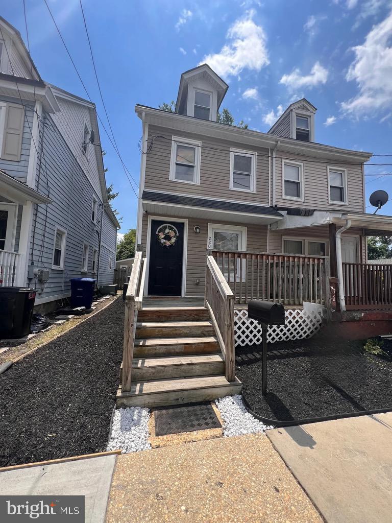 a view of a brick house with wooden deck stairs and a bench