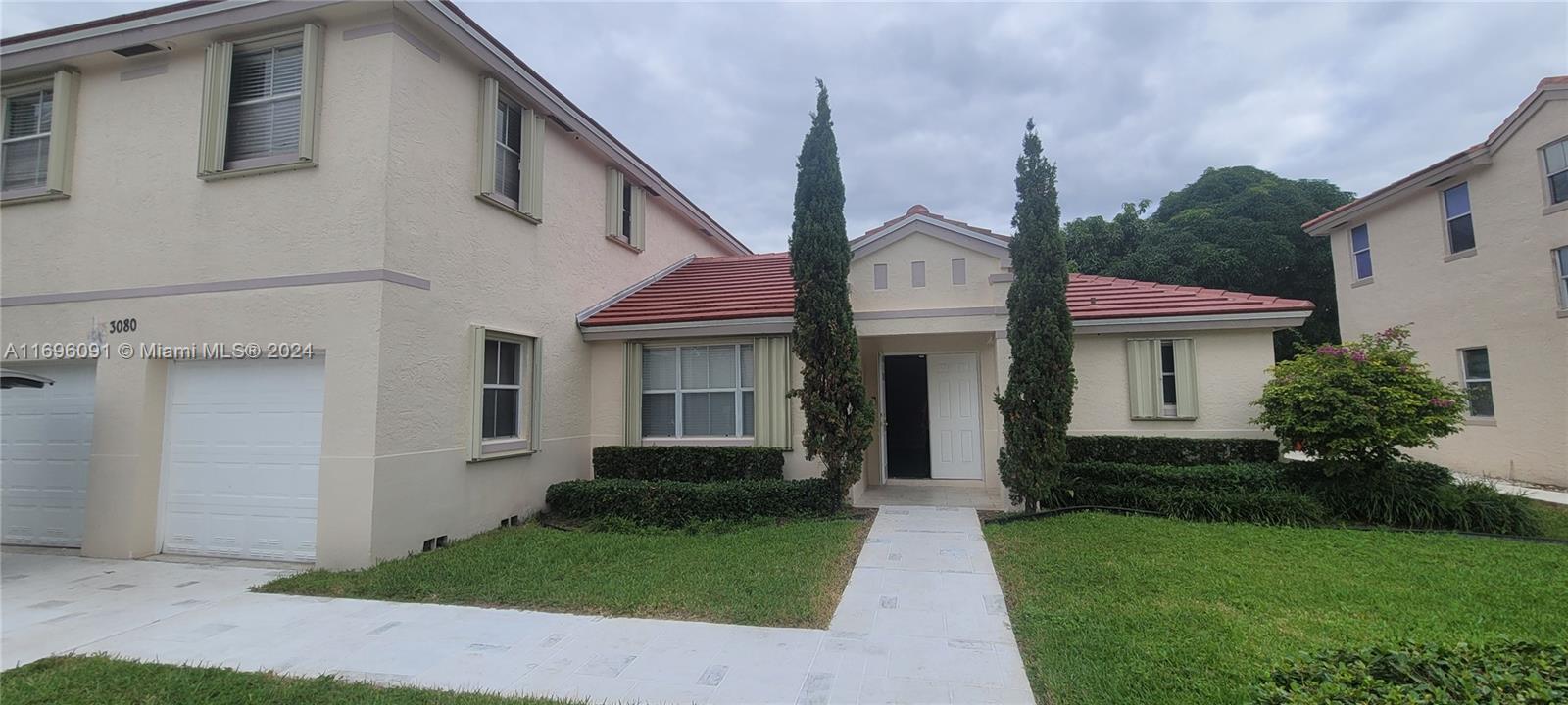 a view of a white house with a small yard plants and a large tree