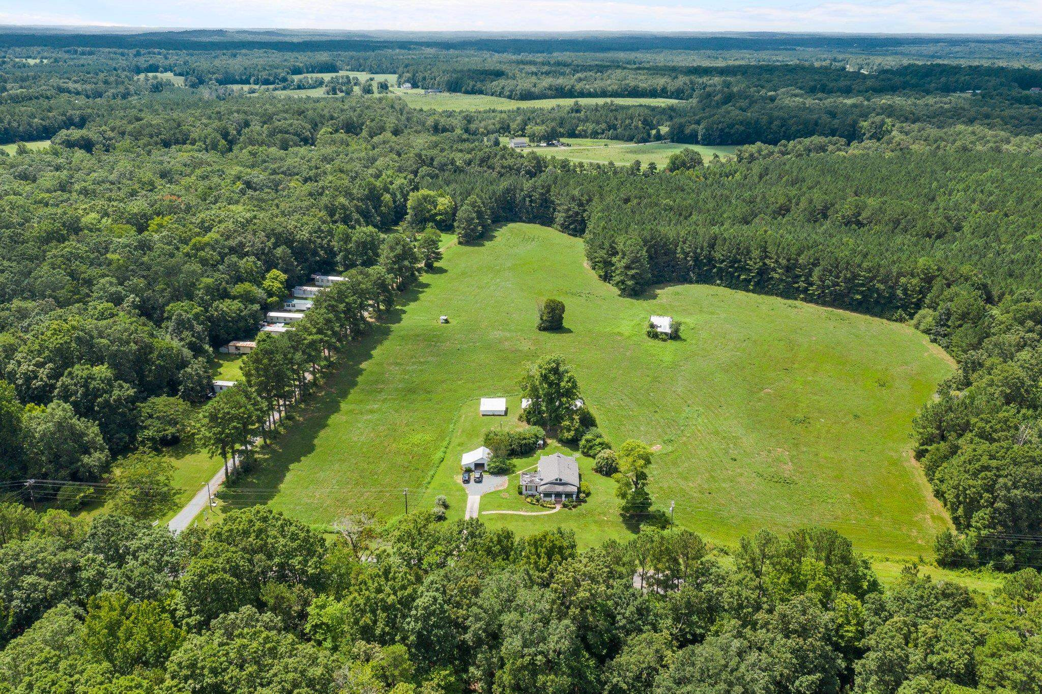 an aerial view of a residential houses with outdoor space and trees all around