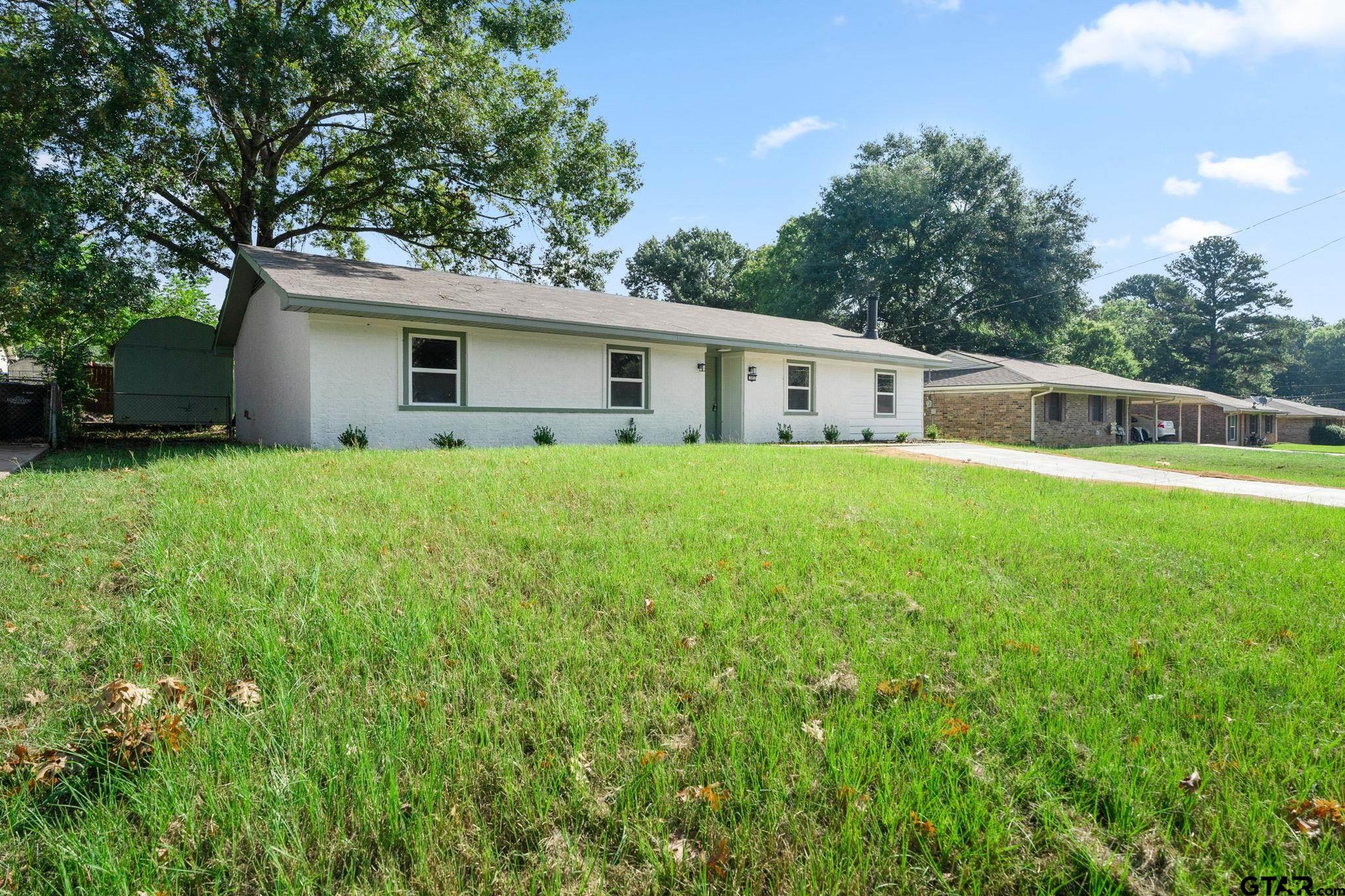 a house that is sitting in the grass with large trees and plants