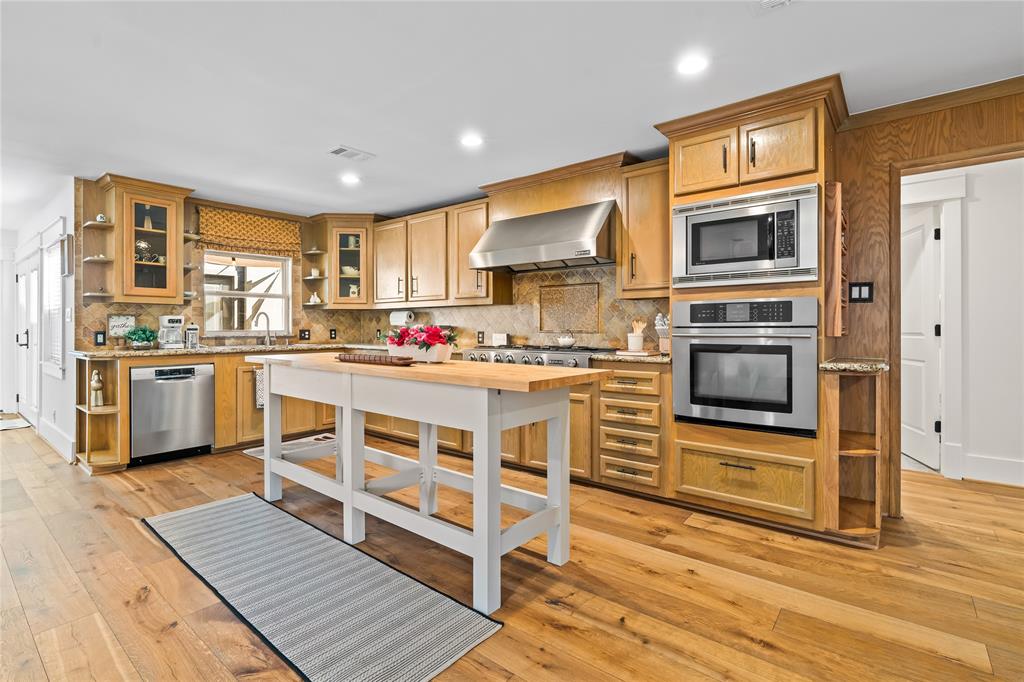 a kitchen with stainless steel appliances a stove a sink dishwasher a refrigerator and white cabinets with wooden floor