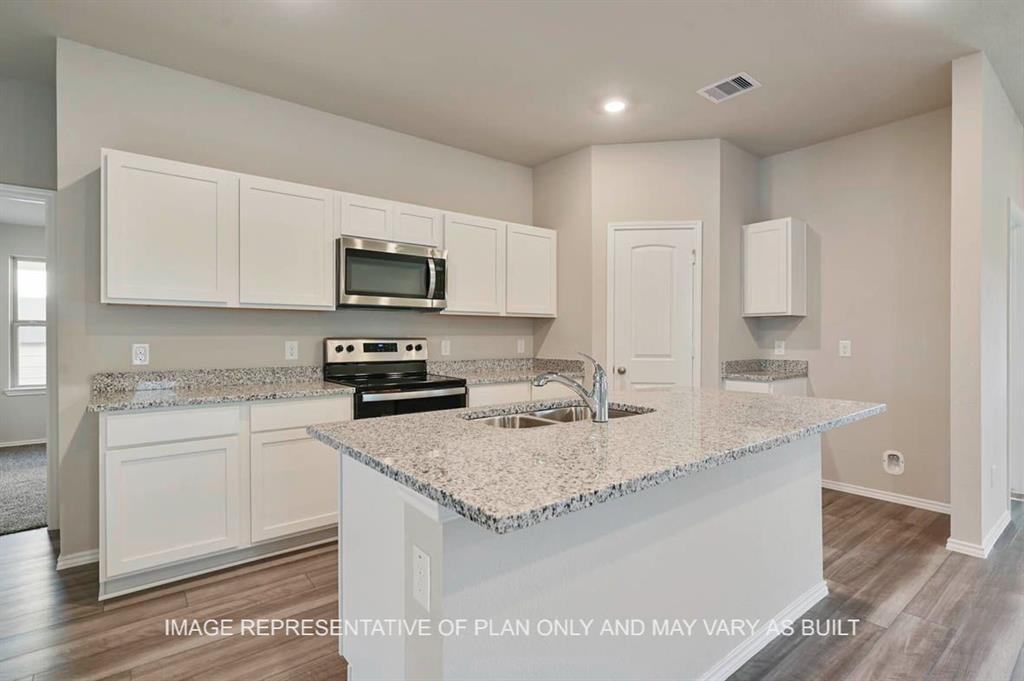 a kitchen with granite countertop a sink a stove top oven and cabinetry