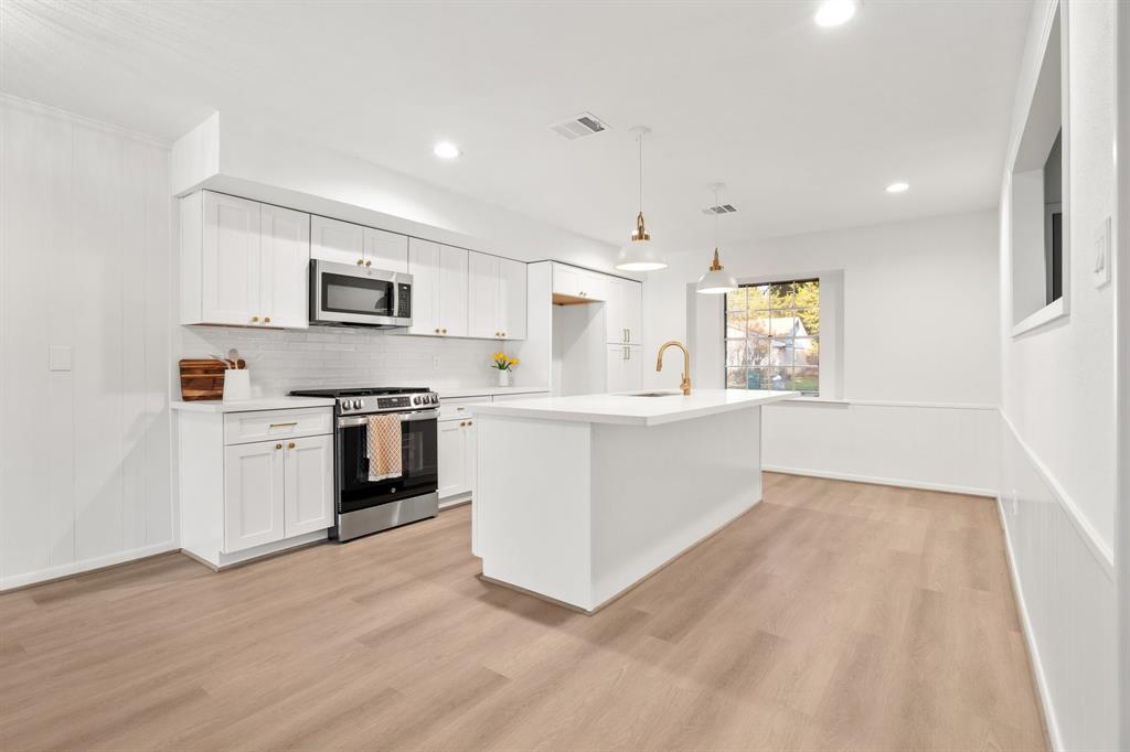 a large kitchen with a stove a sink a microwave a counter space and cabinets