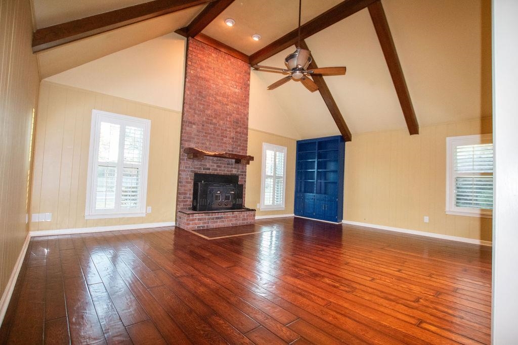 an empty room with wooden floor fireplace and windows