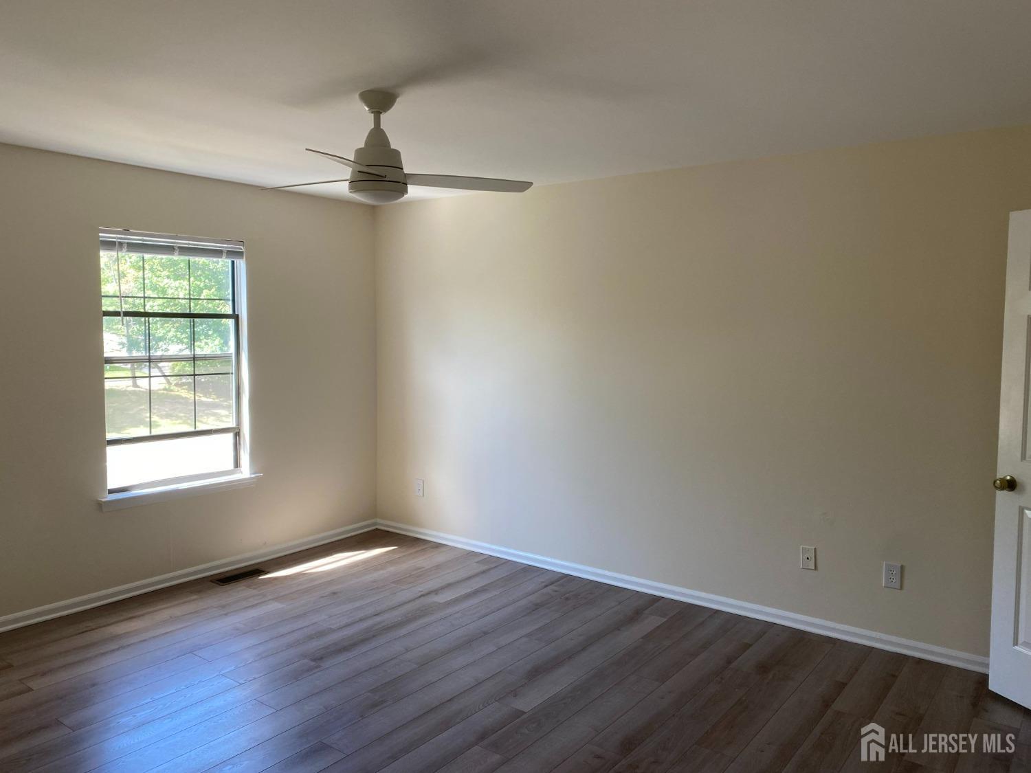 an empty room with wooden floor chandelier fan and windows