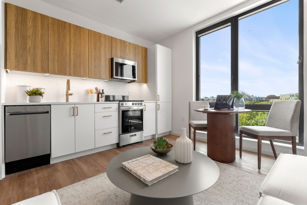 a living room with stainless steel appliances furniture a rug and a kitchen view