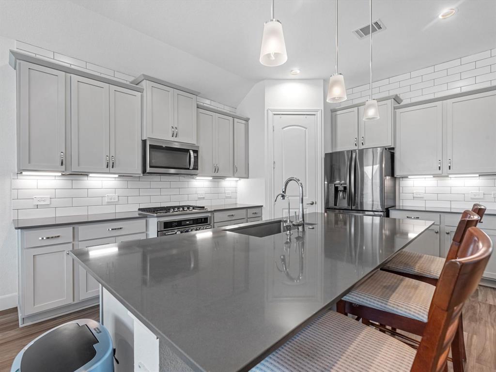 Modern kitchen featuring stainless steel appliances, white subway tile backsplash, gray countertops, and ample cabinet space. Bright with pendant lighting and a sleek design.