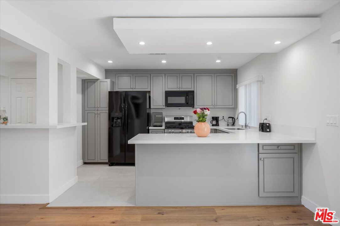 a kitchen with stainless steel appliances granite countertop a refrigerator a sink dishwasher a stove top oven a refrigerator and white cabinets with wooden floor