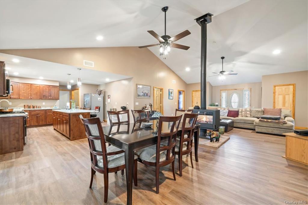 Dining room with light hardwood / wood-style floors, high vaulted ceiling, a wood stove, and ceiling fan