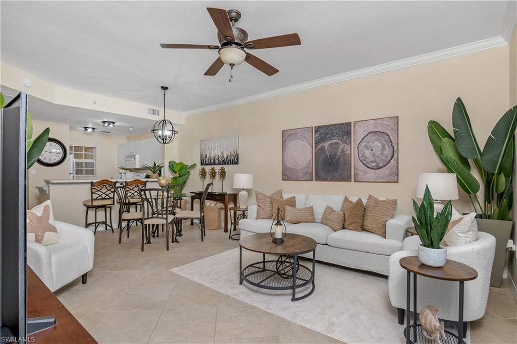 Living room with ceiling fan with notable chandelier, crown molding, and light tile patterned floors