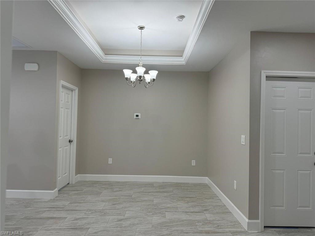 Unfurnished dining area with a chandelier, a raised ceiling, and ornamental molding