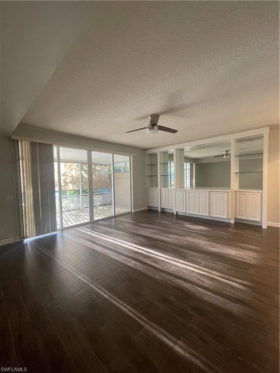 Spare room featuring a textured ceiling, ceiling fan, dark wood-type flooring, and built in features