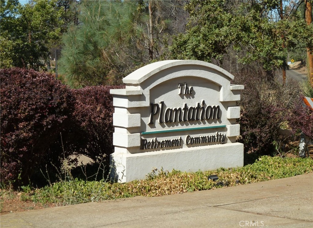 a view of a sign board with flower plants and wooden fence