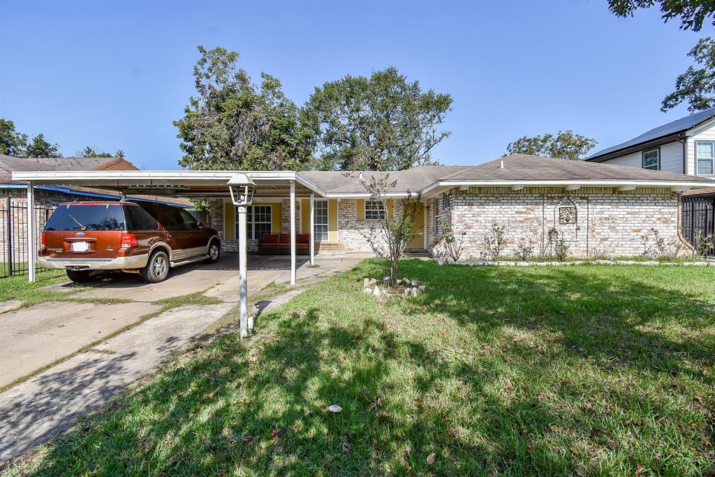 This is a single-story, brick-faced home featuring a carport, a tidy front porch, and a well-sized front lawn. The house has a traditional design with a shingled roof and is situated in a neighborhood with similar properties.