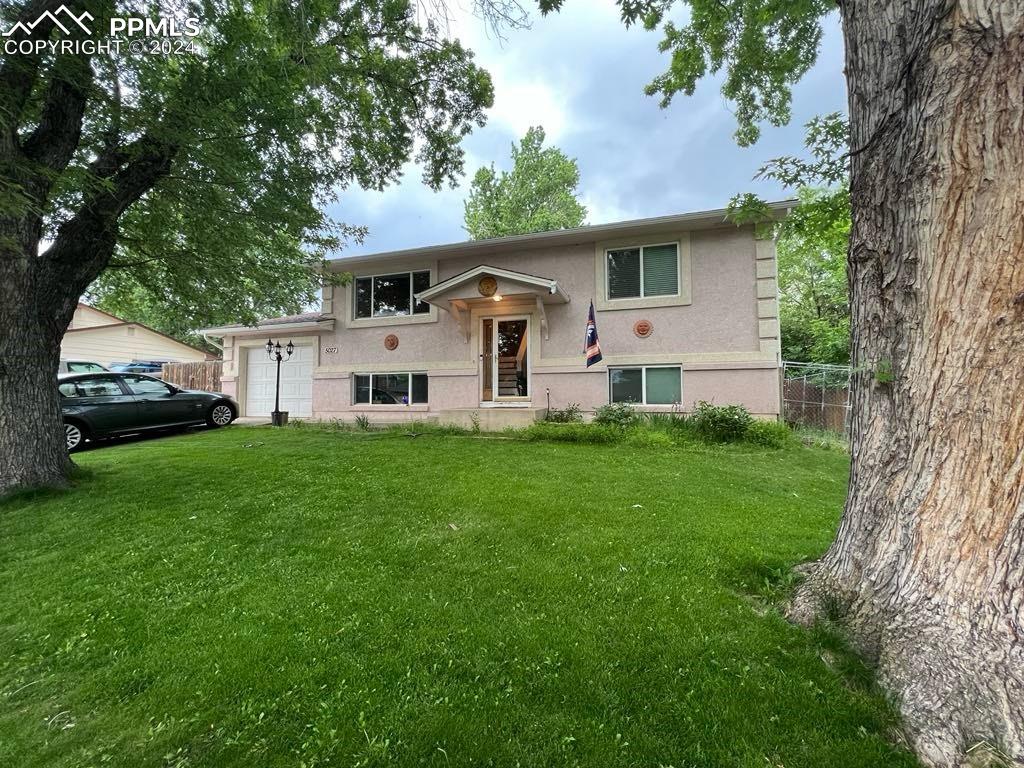 Raised ranch featuring a garage and a front lawn