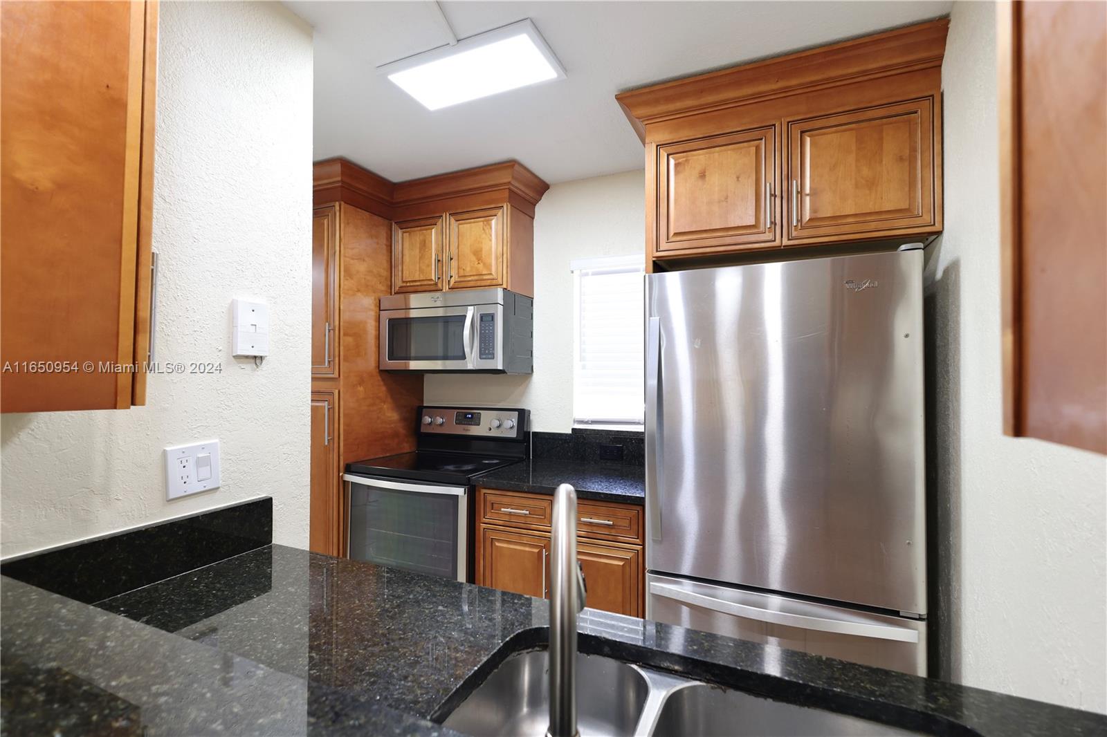 a kitchen with granite countertop a refrigerator a sink and wooden cabinets