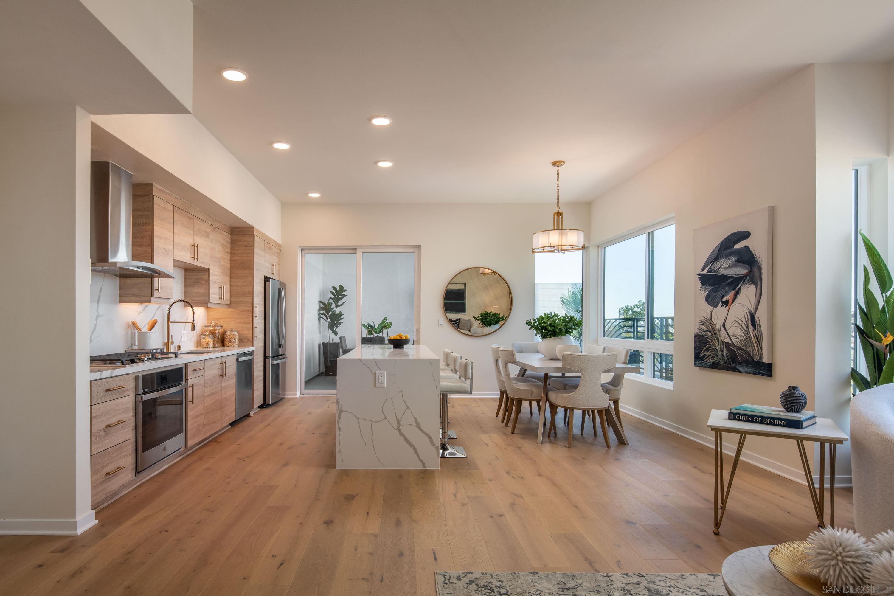 a living room with stainless steel appliances furniture wooden floor and a kitchen view