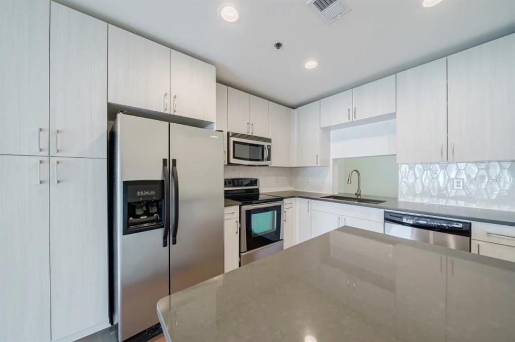 a kitchen with stainless steel appliances kitchen island granite countertop a refrigerator a sink a stove a oven and white cabinets with wooden floor