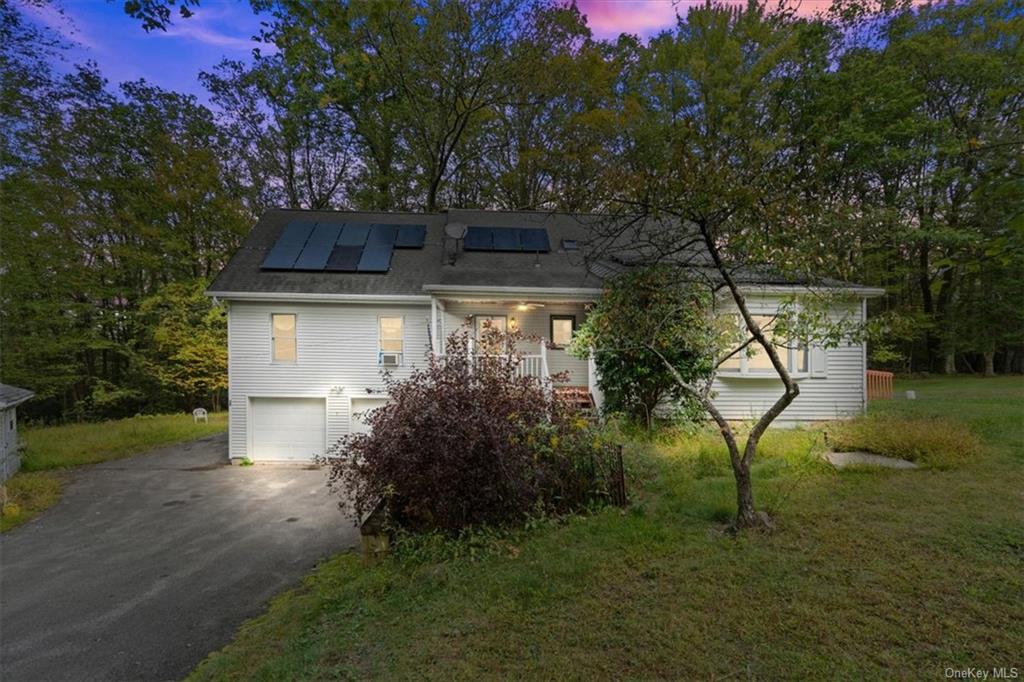 View of front of home with a lawn, a garage, and solar panels