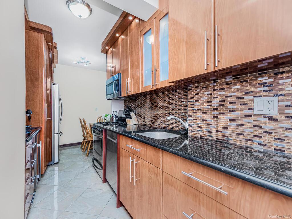 Kitchen featuring appliances with stainless steel finishes, sink, backsplash, dark stone countertops, and light tile patterned floors